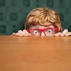 Boy with red glasses hiding behind table