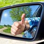 A person sticking their thumb up in the rear-view mirror