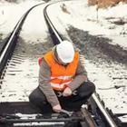 A man in an orange vest and white helmet fixing a railroad track