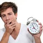 A person yawning and holding a clock