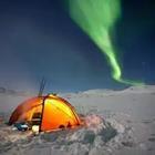 A tent in the snow with a green light in the sky