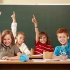 Four children in a classroom raising their hands