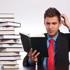 A man in a suit reading a book scratching his head next to a pile of books