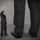 A smaller person in a suit next to a taller person’s leg