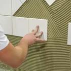 A person putting tile on a green wall