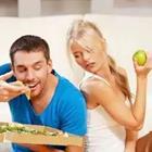 A man eating food and a woman looking at him eating while holding an apple